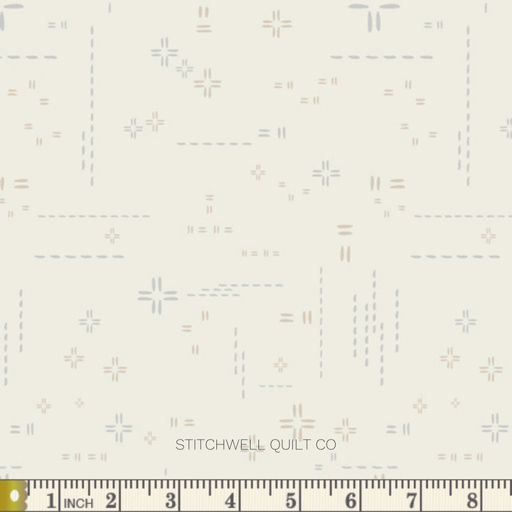 A close-up of fabric with a repeating geometric pattern of small crosses, dashes, and equals signs in muted blue, gray, and taupe on a warm off-white background. A ruler along the bottom edge shows measurements in inches.