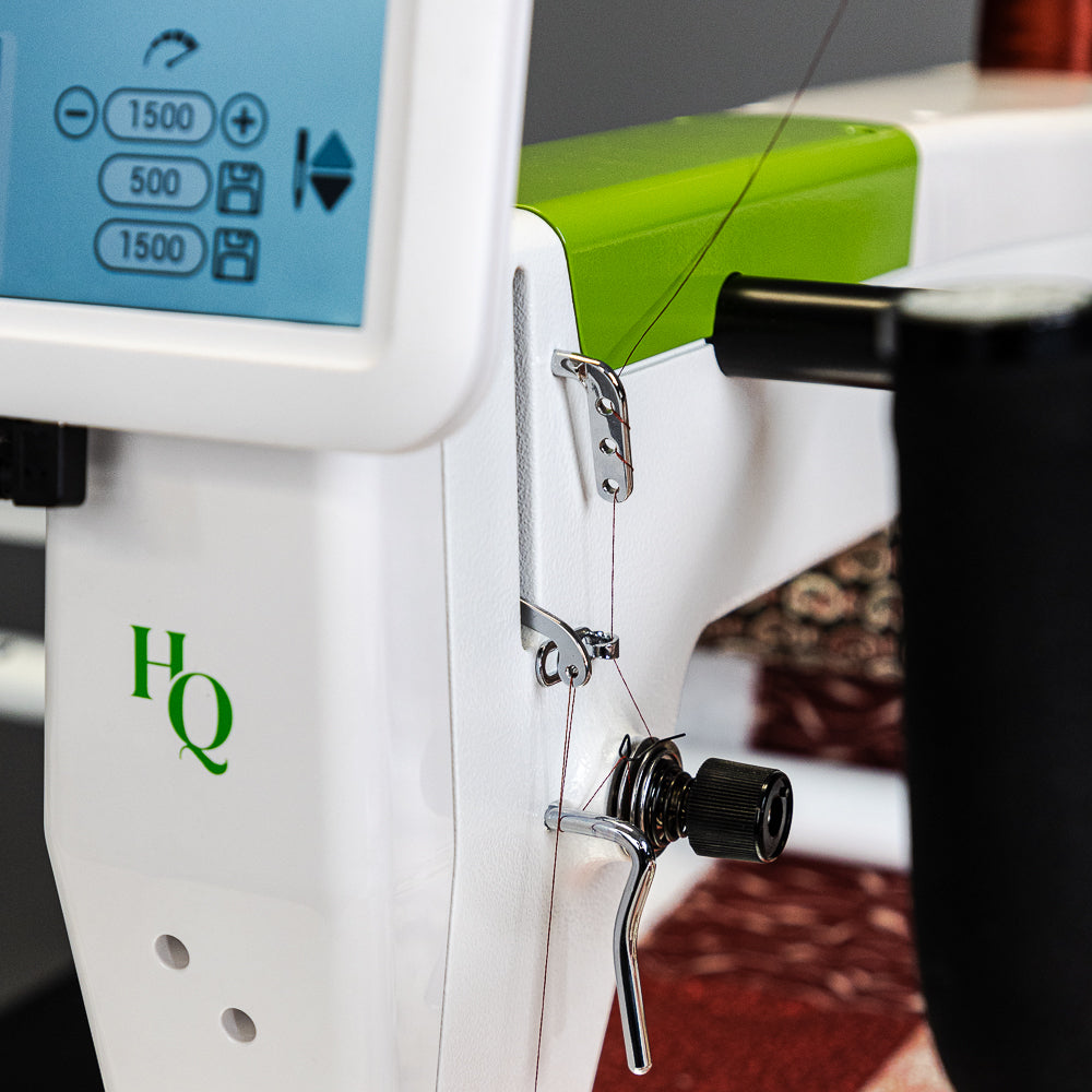 Close-up of a white and green HQ Moxie sewing machine showing the needle area, thread path, and control screen.